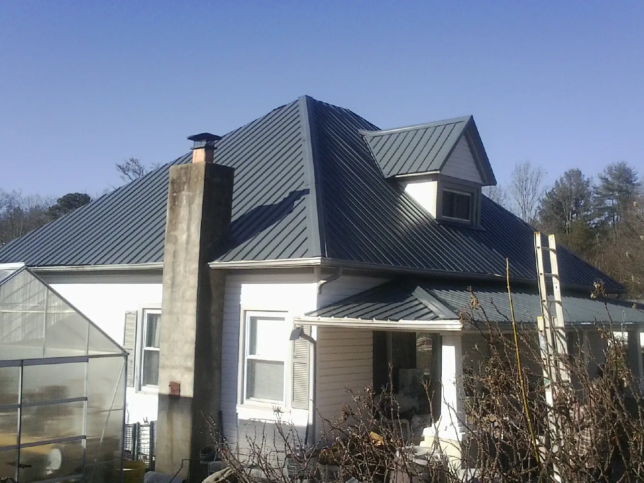 Dark blue standing seam metal roof on a white farmhouse with dormer — Slate & Tile Roof Repair by Roofing Brothers in Burton