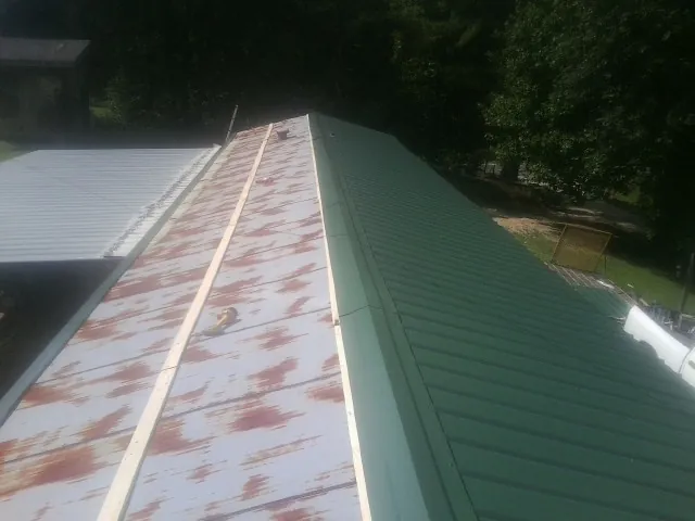 Old rusted panels beside newly installed green metal roofing — Wind Damage Roof Repair by Roofing Brothers in Burton