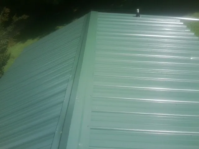 New green metal panels meeting at the ridge of a roof — Flat Roof Repair work by our crew in Burton
